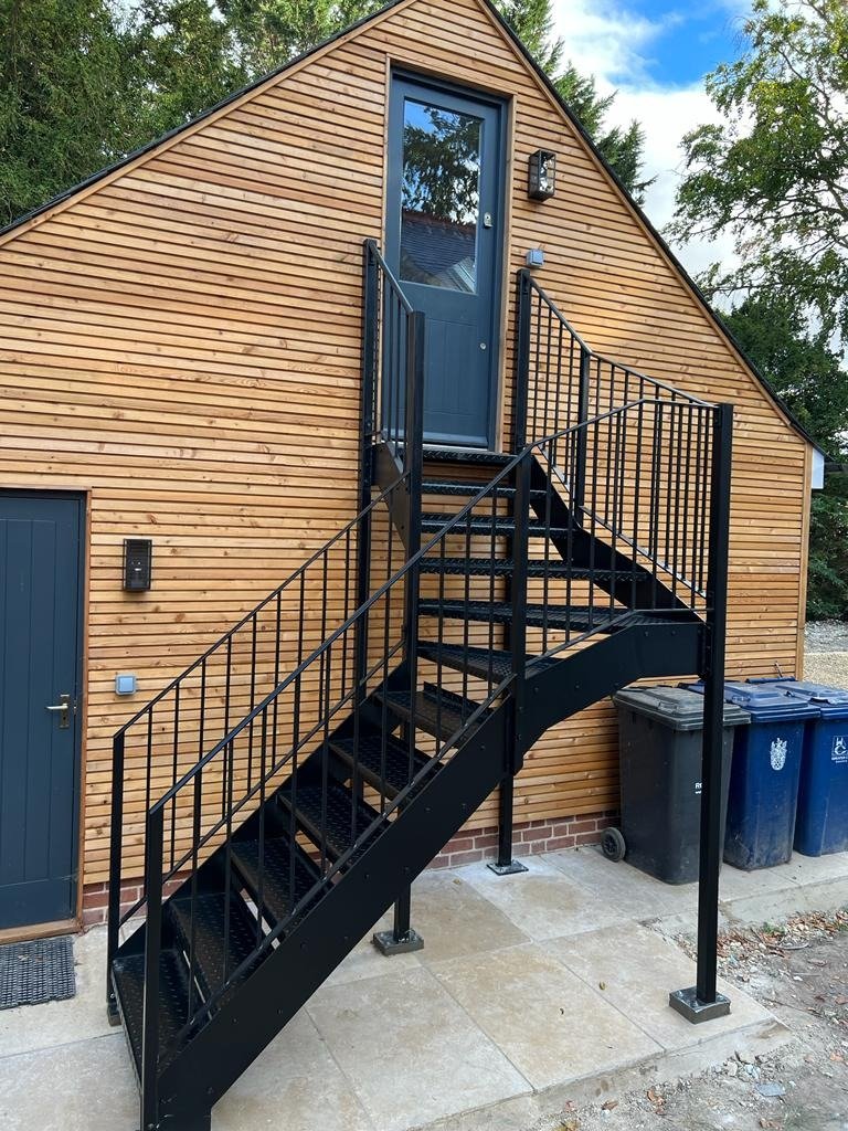 Black steel external staircase with a quarter-turn landing on a timber-clad house