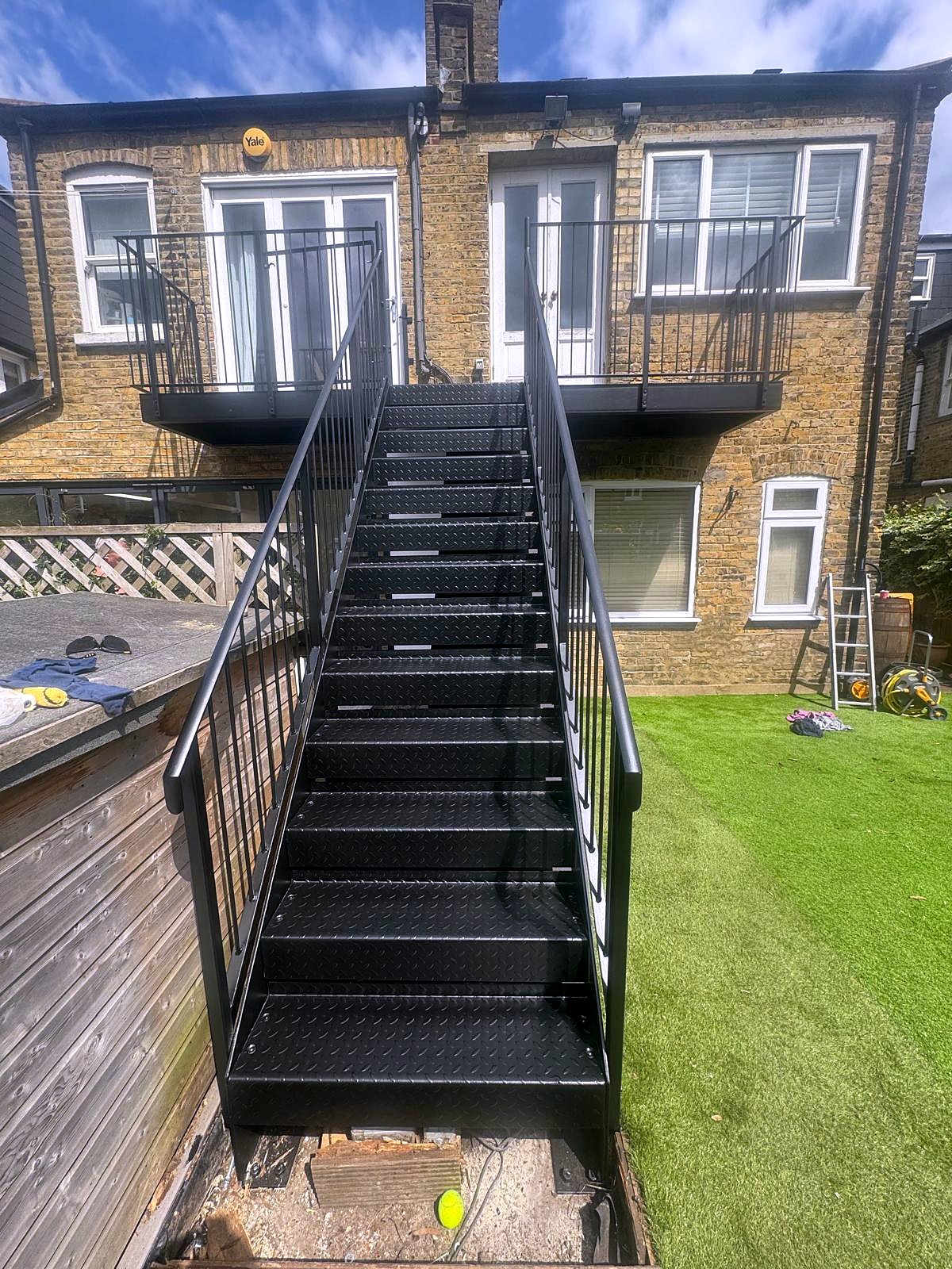 Black steel straight external staircase with railings up to the rear balcony of a brick house